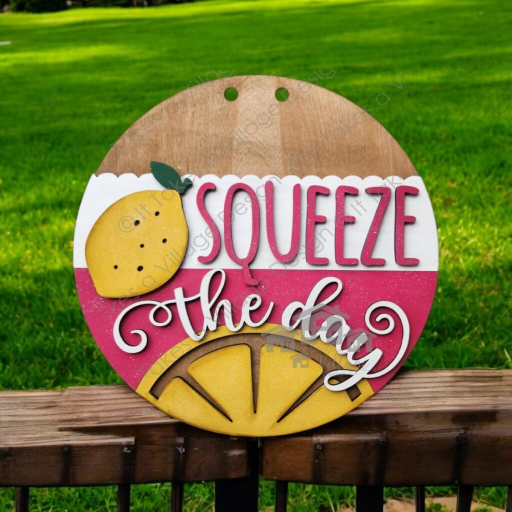 Pink, white, yellow, and green round door hanger with a lemon, lemon slice, and the words "Squeeze the Day" in white.